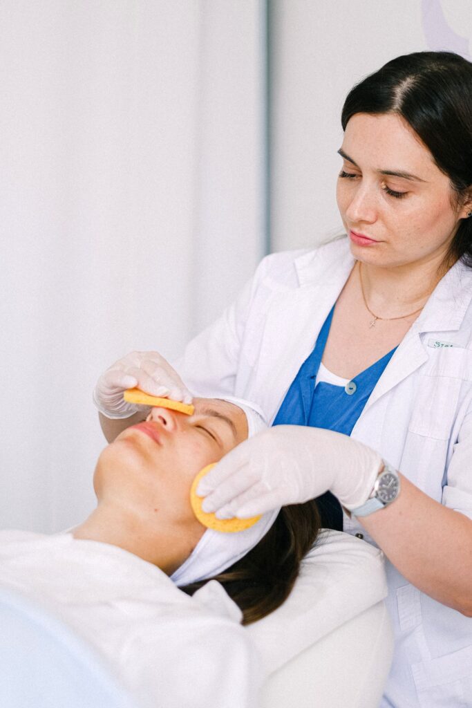 Kosmetyczka oczyszcza skórę twarzy klientki w gabinecie